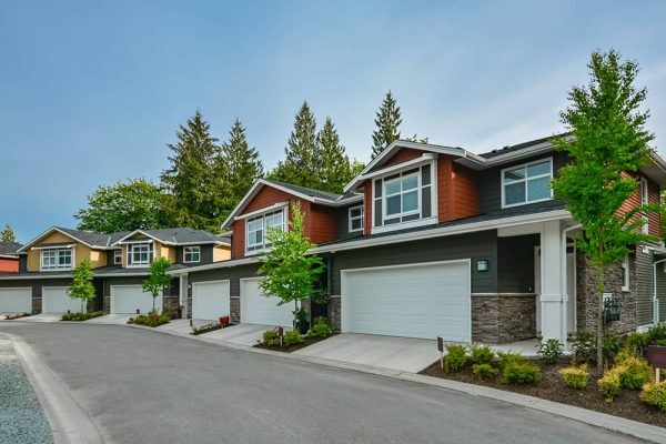 Row of modern townhomes with attached single-car garages, landscaped driveways, and trees in a residential community.