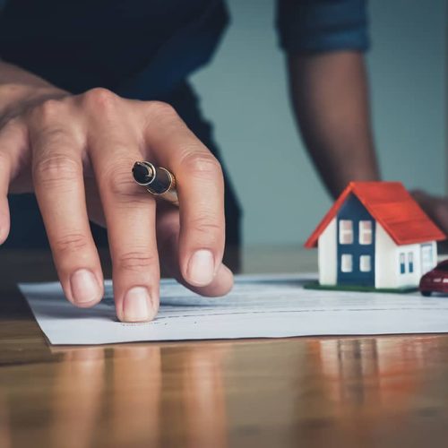 hand holding a pen and a samll house and car toys near