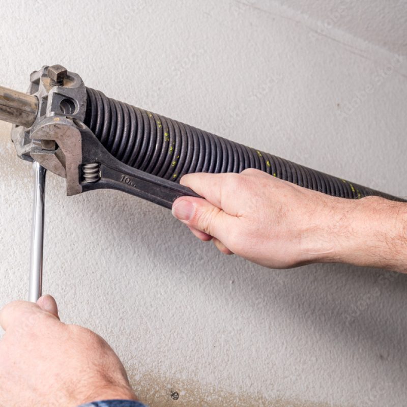 person's hands with a torsion bar and a wrench on a torsion spring that sits on a tube