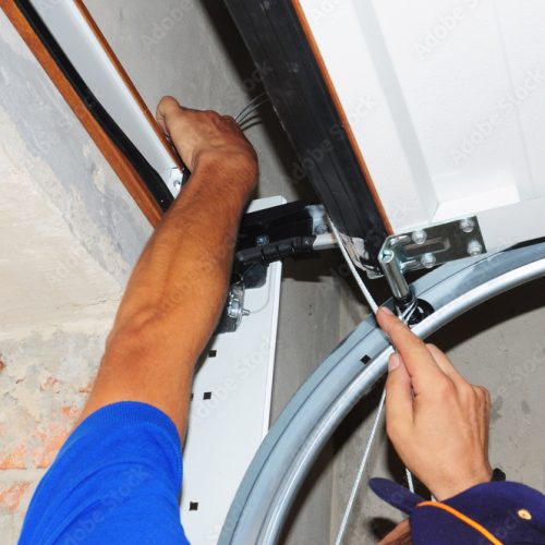 person's hands touching a cable on a garage door in the up position