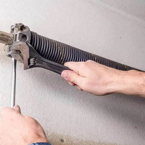 A close-up of a person using a wrench and hex key to adjust or repair a torsion spring on a garage door.